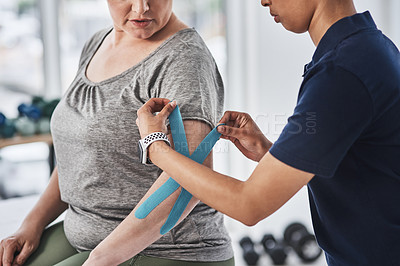 Buy stock photo Shot of an unrecognizable physiotherapist putting kinesiology tape on a patient's arm at a clinic