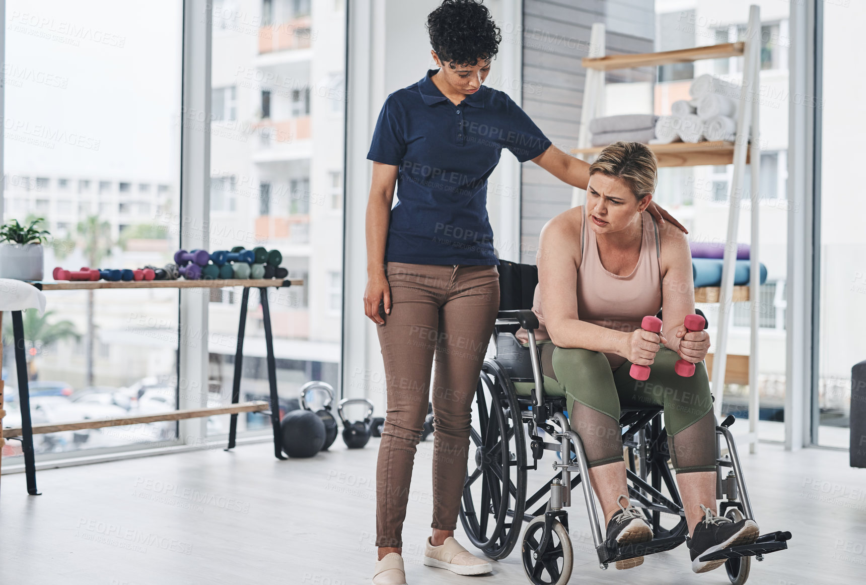 Buy stock photo Full length shot of a young physiotherapist helping her wheelchair bound patient exercise with dumbbells at a clinic