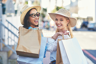 Buy stock photo Cropped portrait of two attractive young girlfriends smiling while walking with shopping bags in the city during the day