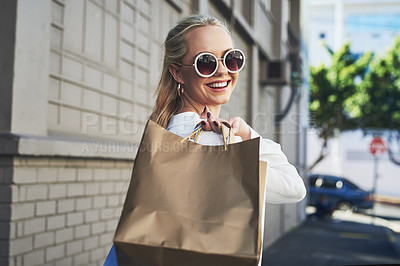 Buy stock photo Cropped portrait of an attractive young woman smiling while holding shopping bags in the city during the day