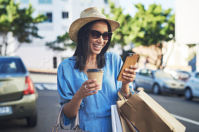 Buy stock photo Cropped shot of an attractive young woman smiling while using a smartphone after a shopping spree in the city