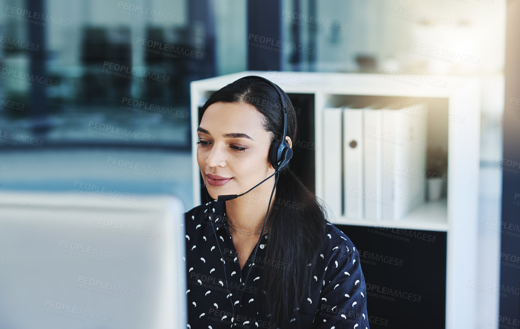 Buy stock photo Cropped shot of an attractive young businesswoman wearing a headset and using her computer while sitting in the office alone