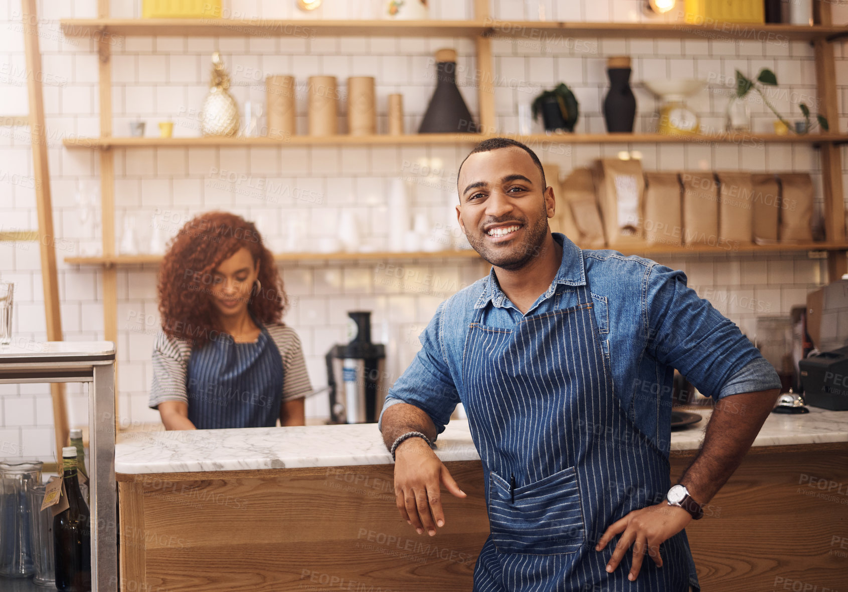 Buy stock photo Cropped shot of a handsome young businessman standing in his cafe while a barista works behind him