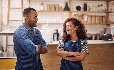 Buy stock photo Cropped shot of two young business owners standing in their cafe with their arms folded while looking at each other