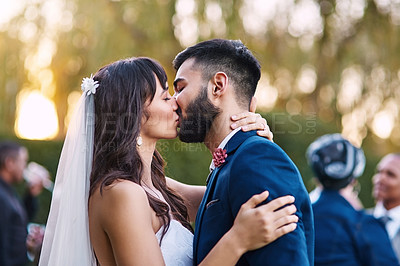 Buy stock photo Cropped shot of an affectionate young newlywed couple kissing passionately on their wedding day with their guests in the background