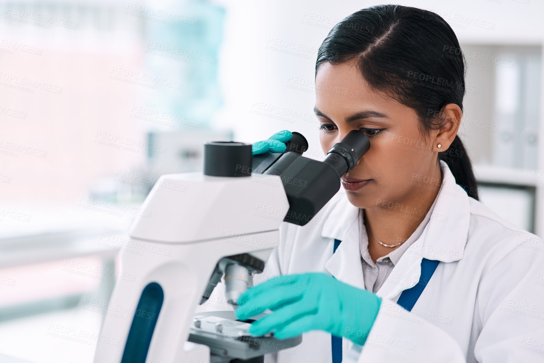 Buy stock photo Cropped shot of an attractive young female scientist looking through a microscope while working in a laboratory