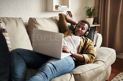 Buy stock photo Cropped shot of a handsome young man using a laptop while listening to music on his headphones in his living room at home