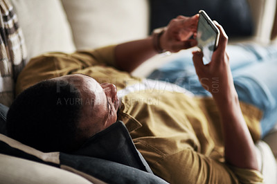 Buy stock photo Cropped shot of a handsome young man using a smartphone while relaxing on his couch at home
