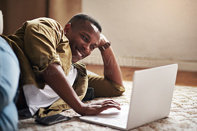 Buy stock photo Cropped shot of a handsome young man smiling while using a laptop in his living room at home