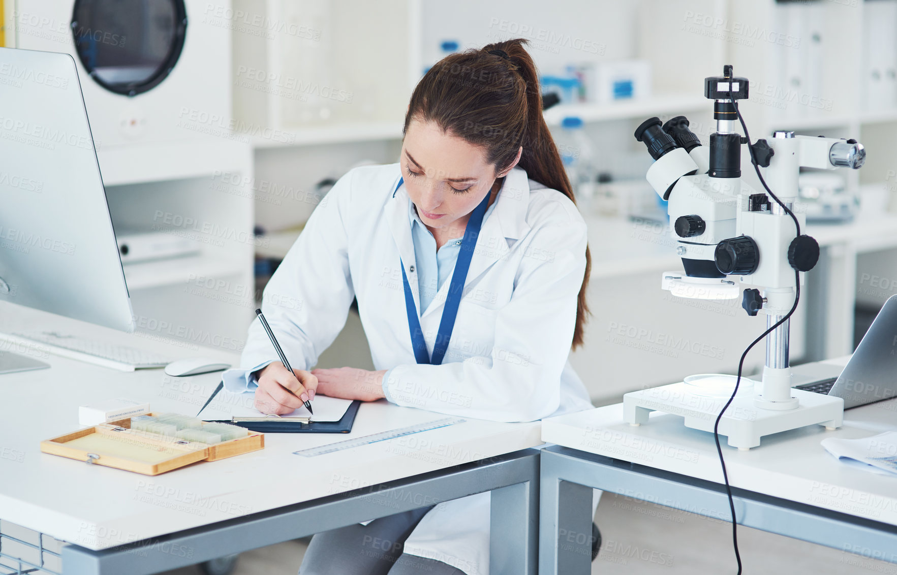 Buy stock photo Cropped shot of a focused young female scientist making notes in a book while doing tests inside of a laboratory during the day