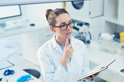Buy stock photo Cropped shot of a focused young female scientist reading from her notebook while contemplating inside of a laboratory