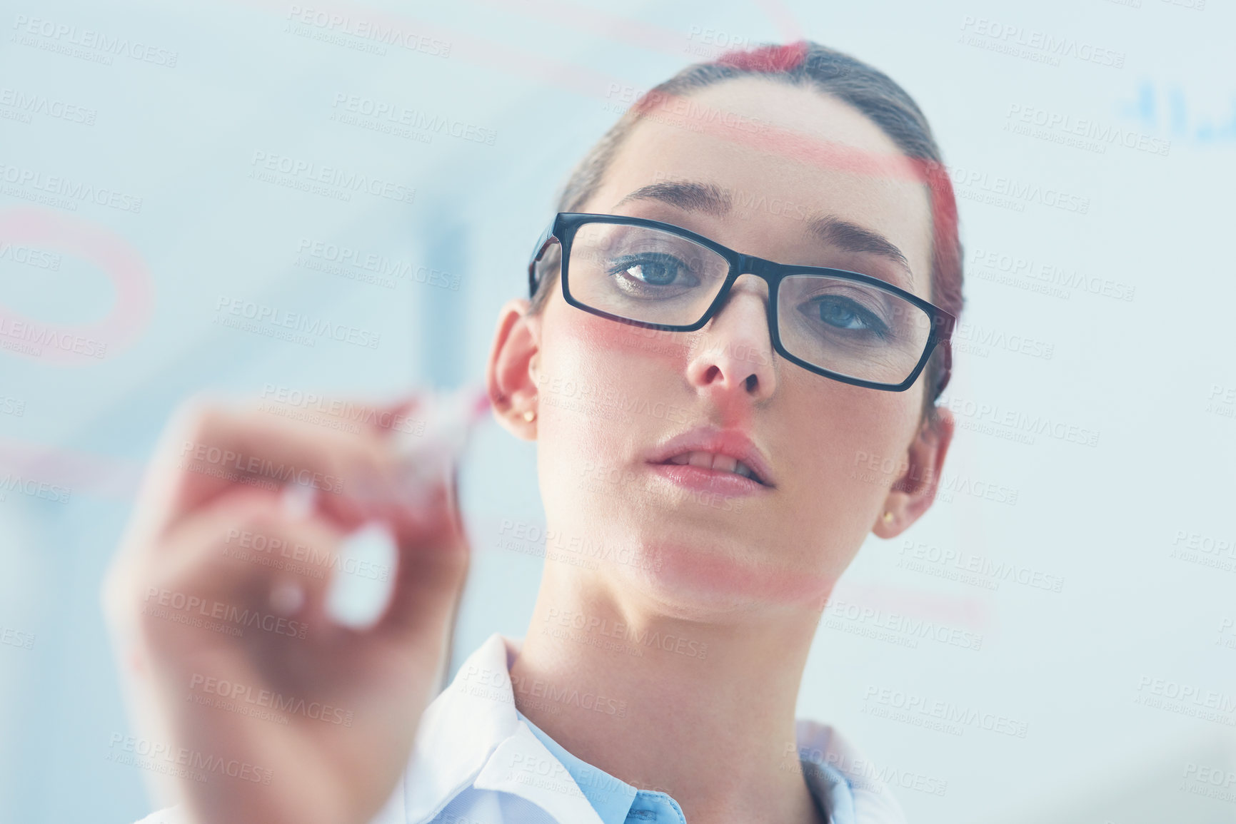 Buy stock photo Closeup of a focused young female scientist doing calculations and writing out formulas on a glass wall inside of a laboratory