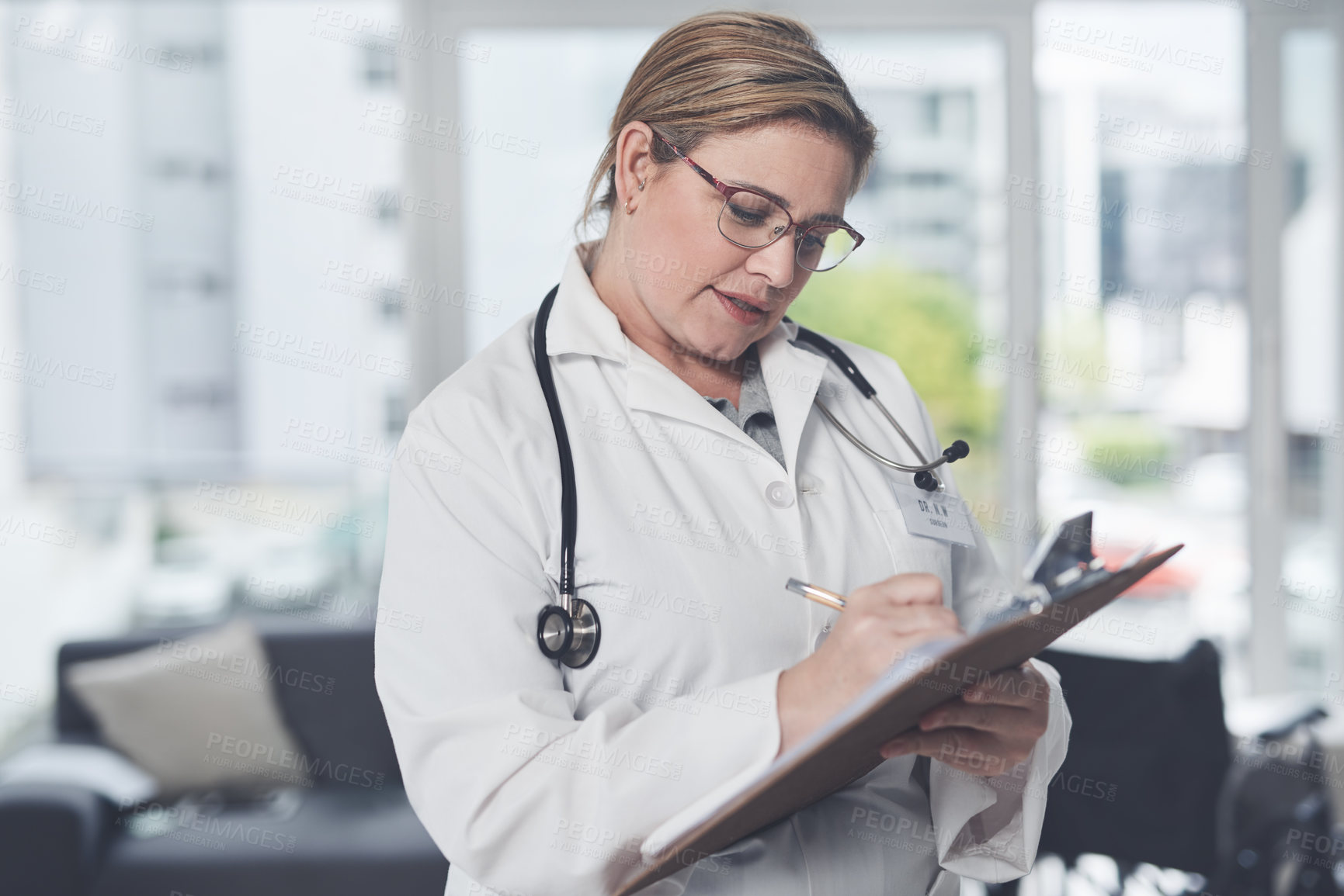 Buy stock photo Cropped shot of an attractive young female doctor writing on a clipboard while standing in her office