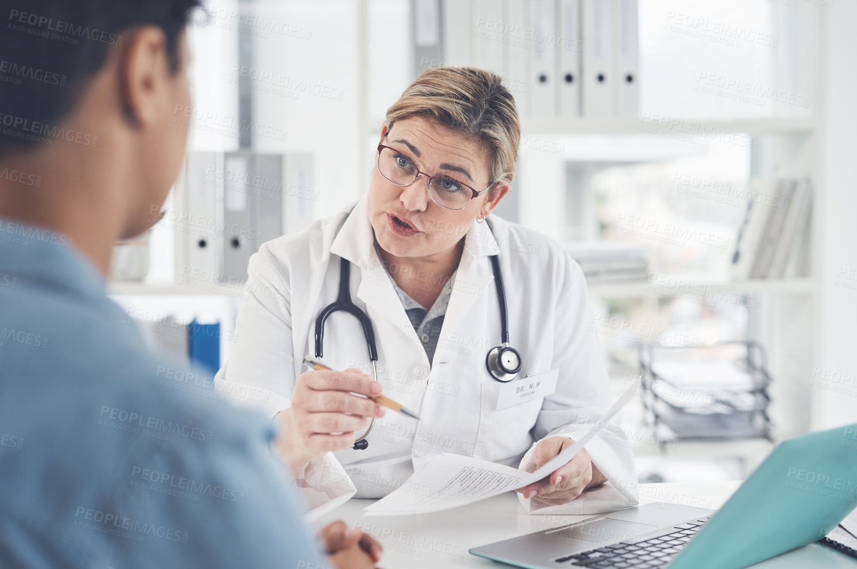 Buy stock photo Cropped shot of an attractive young female doctor holding a document while having a discussion with a female patient in her office