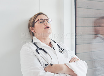 Buy stock photo Cropped shot of an attractive young female doctor looking exhausted while leaning against a wall in her office