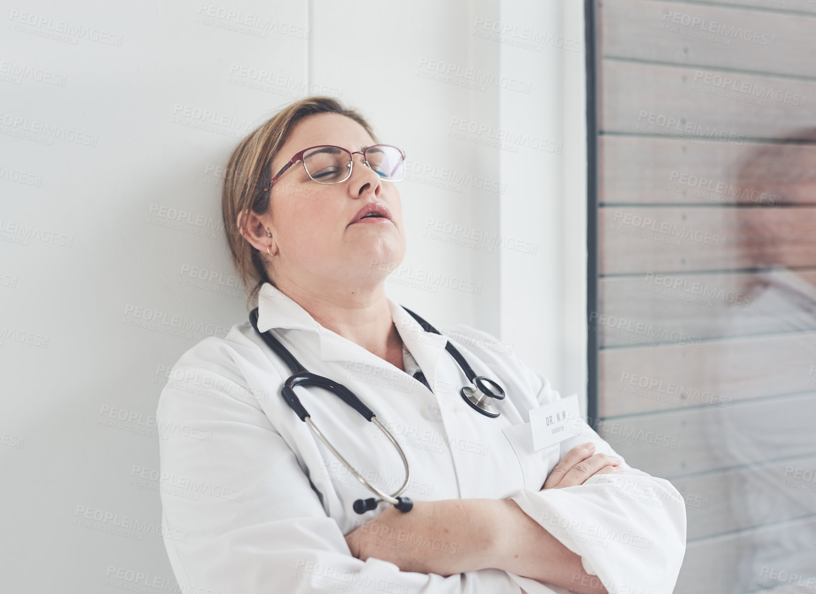 Buy stock photo Cropped shot of an attractive young female doctor looking exhausted while leaning against a wall in her office