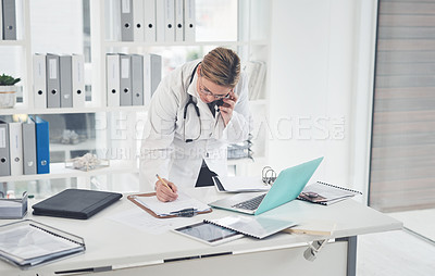 Buy stock photo Cropped shot of an attractive young female doctor writing on a clipboard while taking a phonecall in her office
