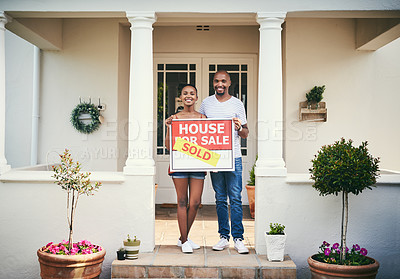 Buy stock photo Shot of a young couple standing in front of their new home with a sold real estate sign