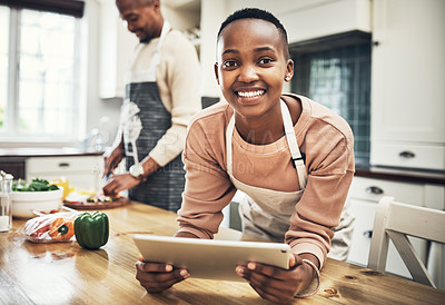 Buy stock photo Cropped portrait of an attractive young woman using a tablet in the kitchen while her husband cooks in the background