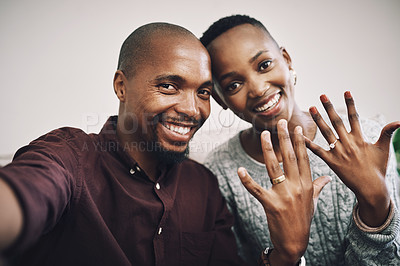 Buy stock photo Portrait of a happy newly engaged young couple taking selfies and showing their engagement rings at home