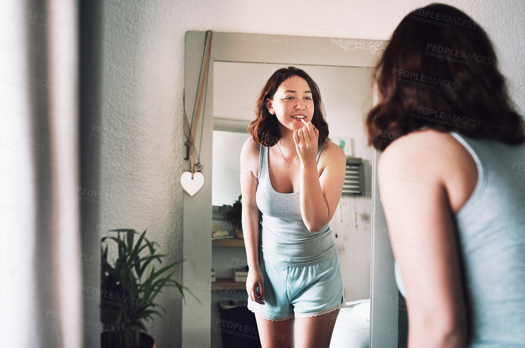 Buy stock photo Cropped shot of an attractive young woman applying lipstick while standing in front of the mirror in her bedroom at home