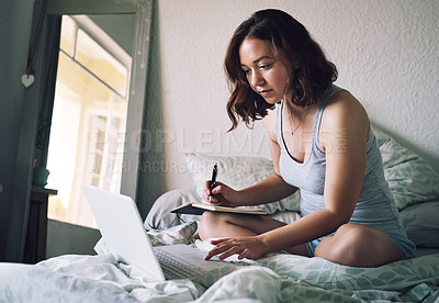 Buy stock photo Full length shot of an attractive young woman writing in a notebook while using a laptop in her bedroom at home