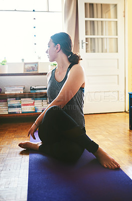 Buy stock photo Cropped shot of an attractive young woman sitting and holding a spinal half twist while doing yoga in her home