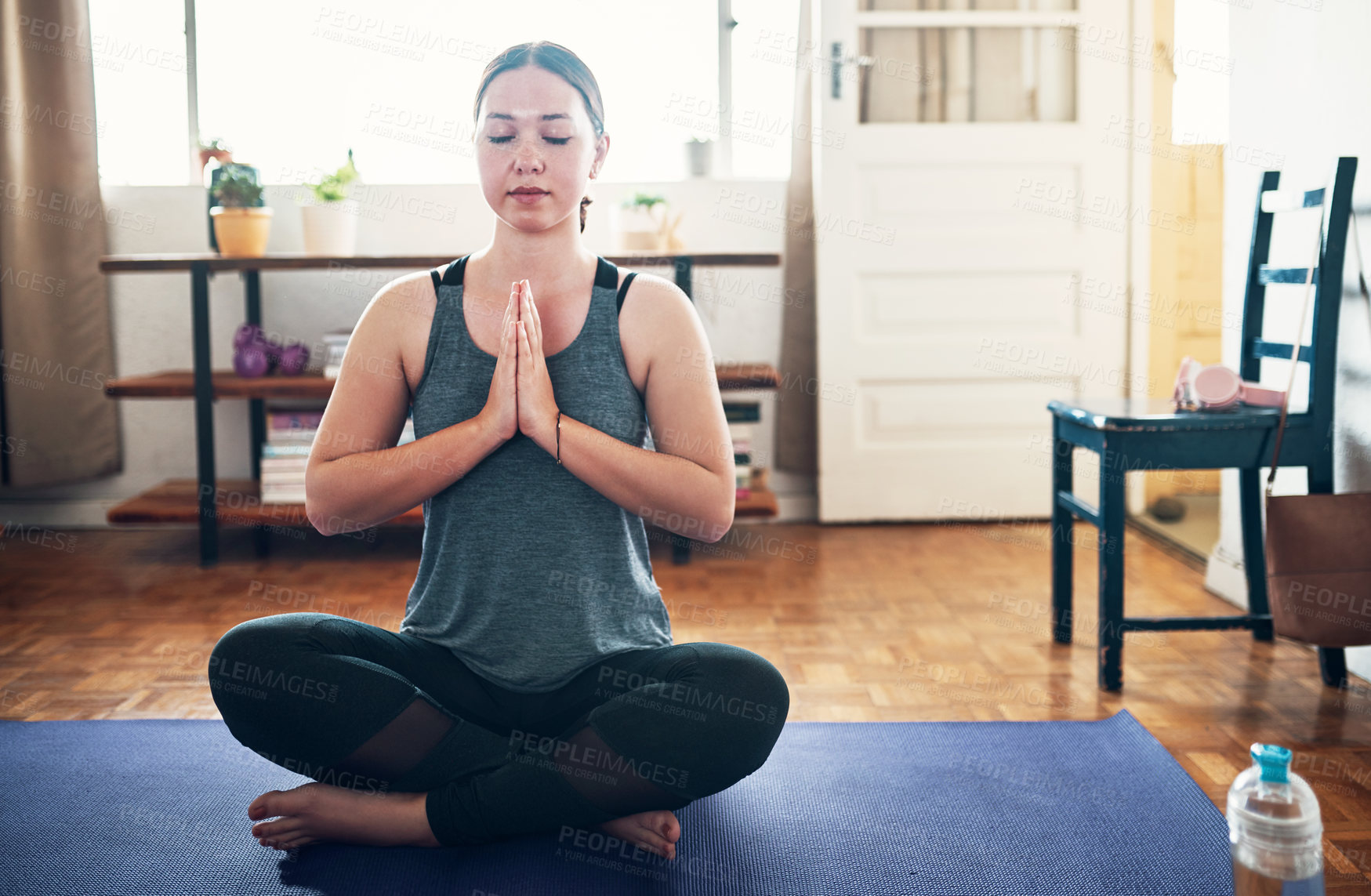 Buy stock photo Cropped shot of an attractive young woman sitting on a yoga mat and meditating alone in her home