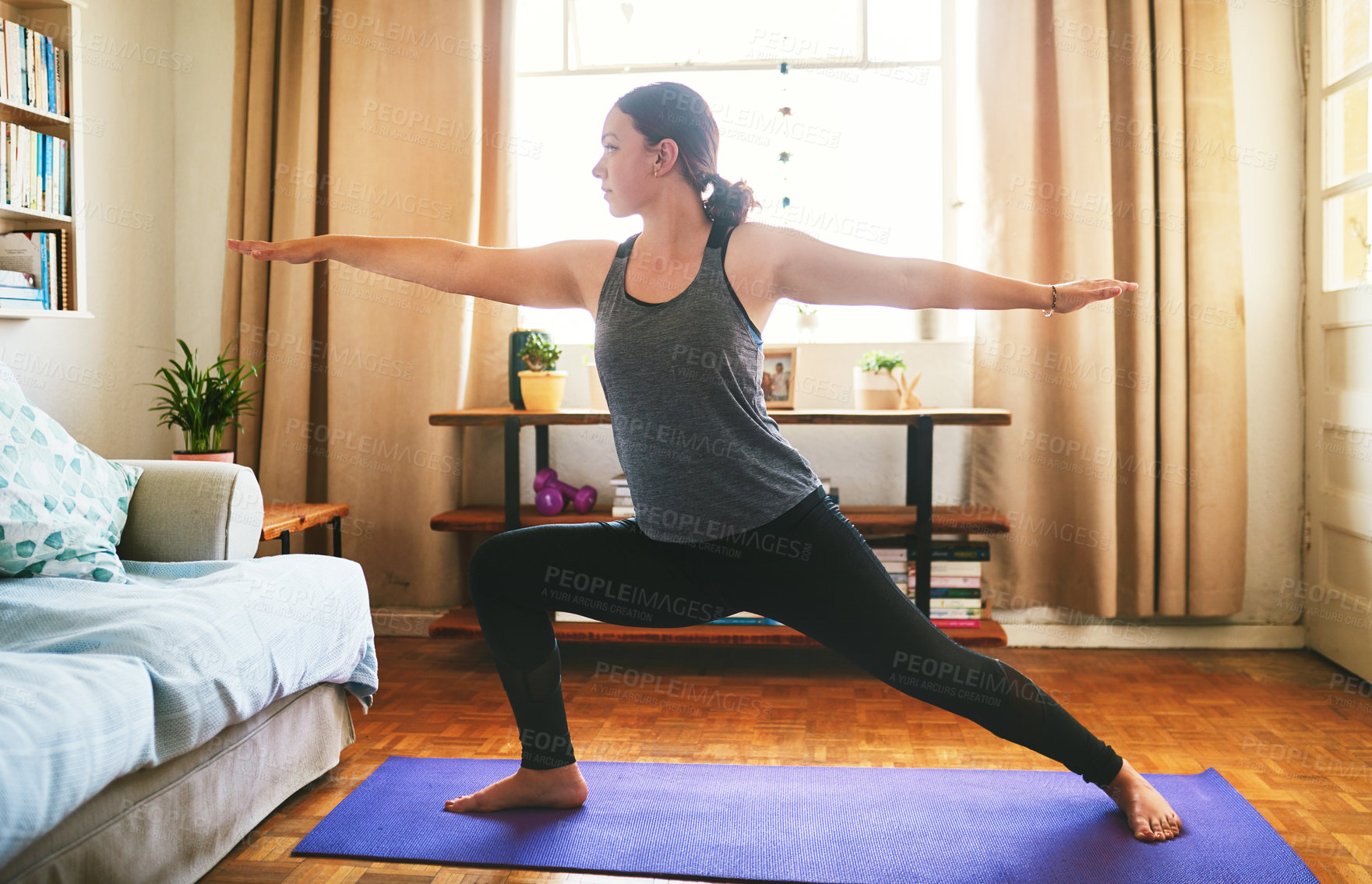 Buy stock photo Cropped shot of an attractive young woman standing and holding a warrior pose while doing yoga in her home
