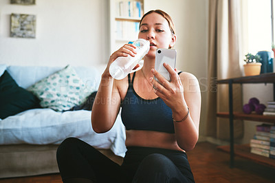 Buy stock photo Cropped shot of an attractive young woman sitting and drinking water while using her cellphone after a workout
