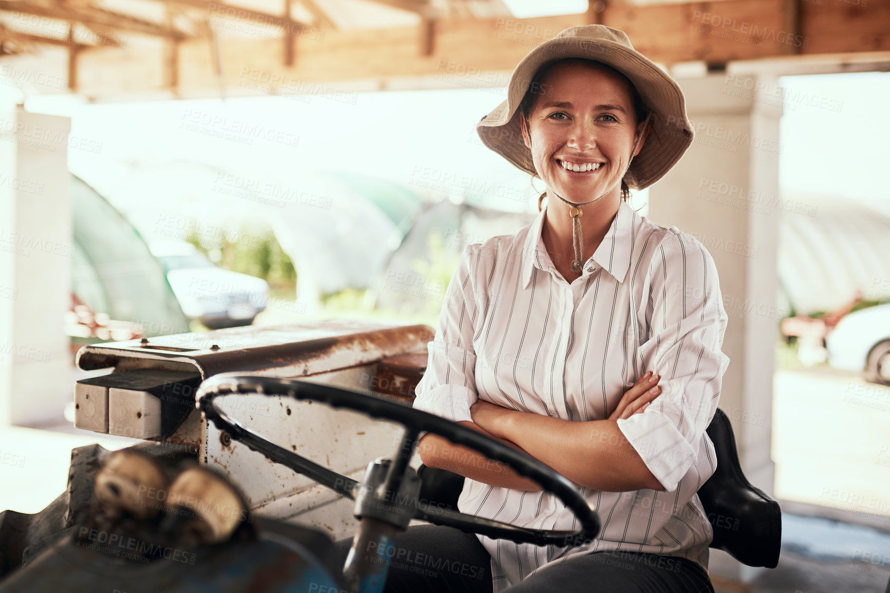 Buy stock photo Portrait of an attractive young female farmer posing with her arms folded while siting inside a tractor at her farm