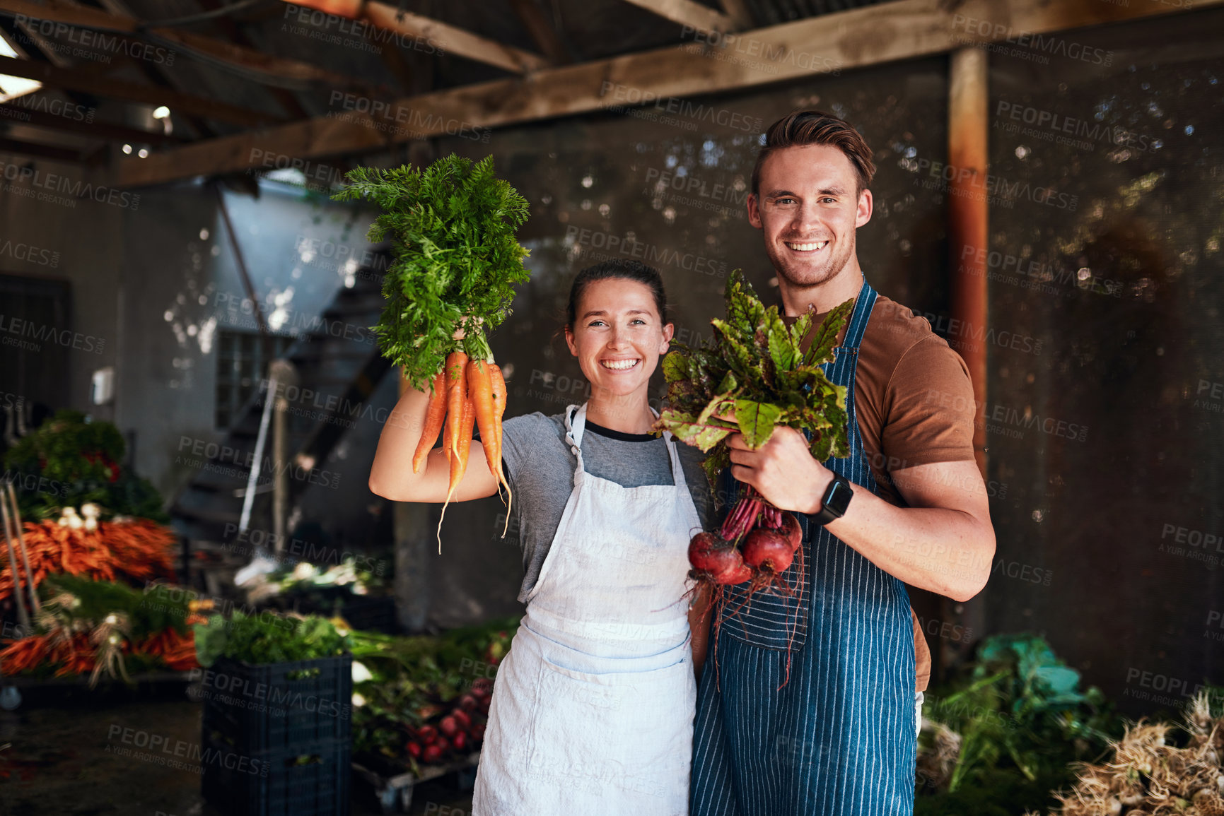 Buy stock photo Portrait of a happy young couple posing together holding bunches of freshly picked carrots and beetroot at their farm