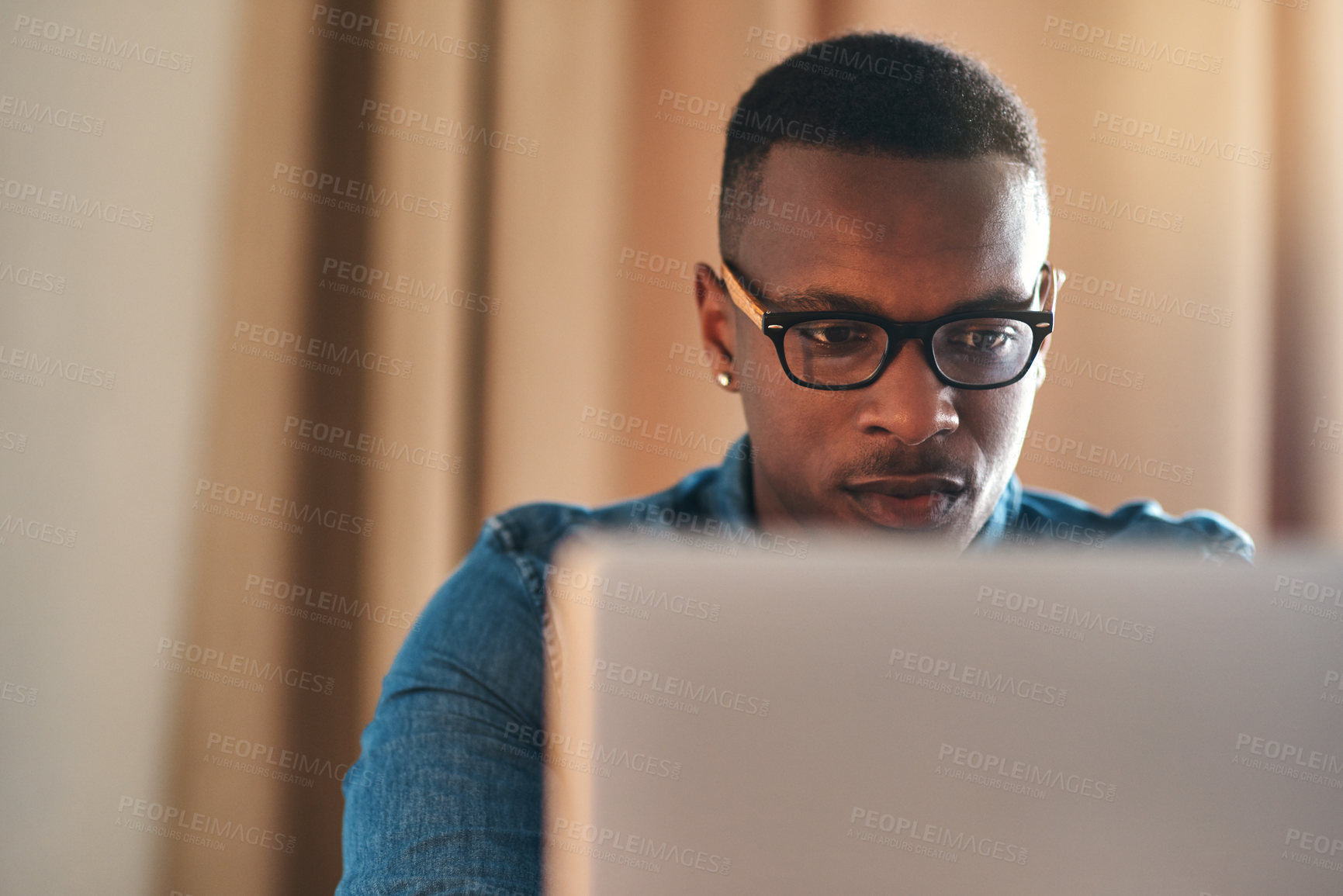 Buy stock photo Focused, serious and confident entrepreneur typing on a laptop and reading an email sitting alone in his home office. African american businessman planning and remote working his startup business