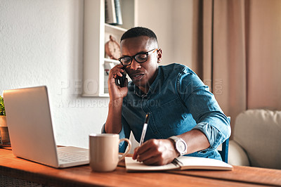 Buy stock photo Young serious professional businessman talking on phone call, writing and sitting with digital laptop at home office. African american employee working and consulting in new company startup