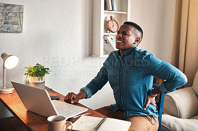 Buy stock photo Cropped shot of a handsome young businessman sitting alone in his office and suffering from back pain