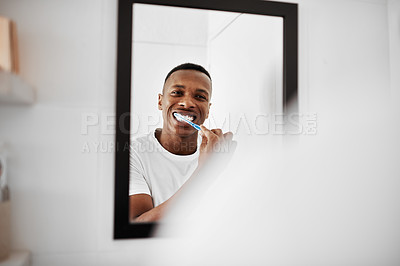 Buy stock photo Shot of a young man brushing his teeth while looking into the bathroom mirror