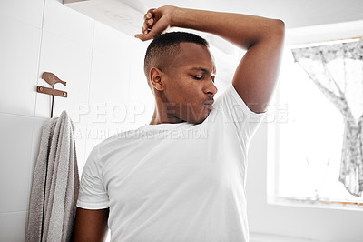 Buy stock photo Shot of a young man smelling his underarms while standing in the bathroom