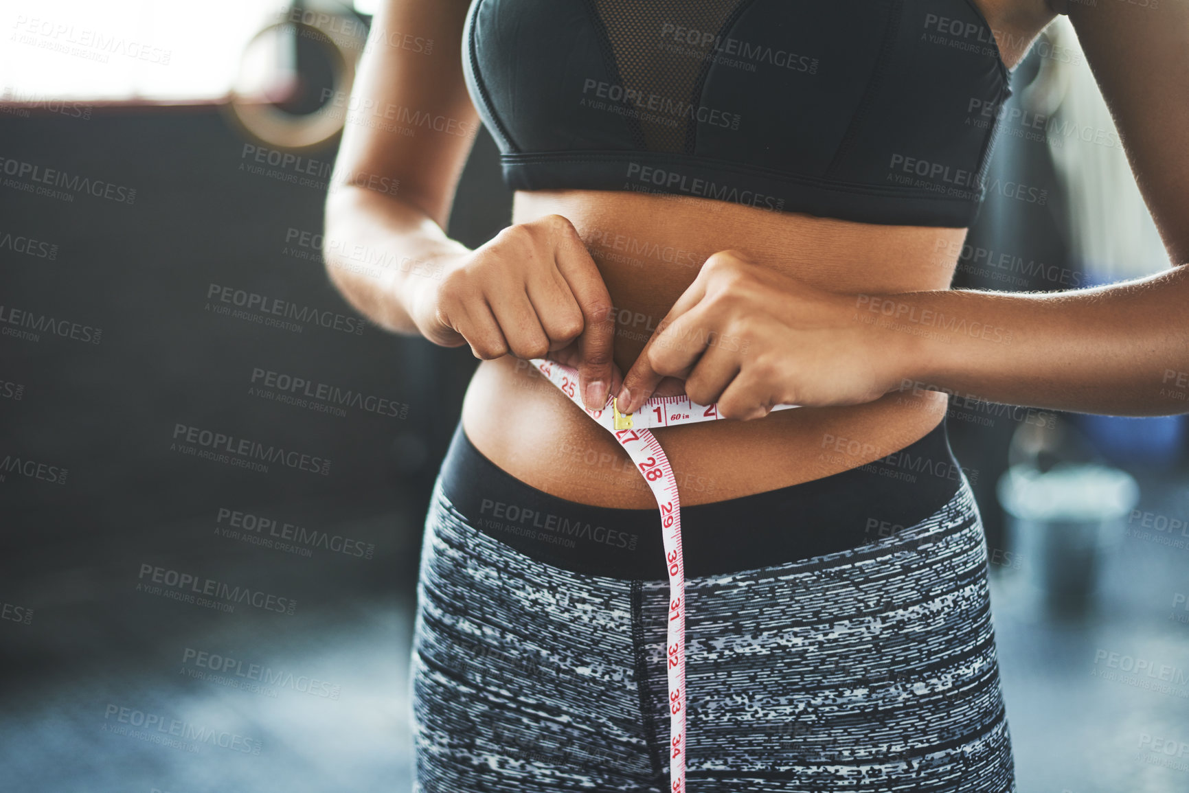 Buy stock photo Cropped shot of a fit young woman measuring her waist in a gym