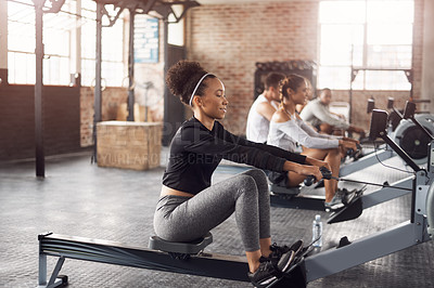 Buy stock photo Shot of a young woman working out with a rowing machine in the gym
