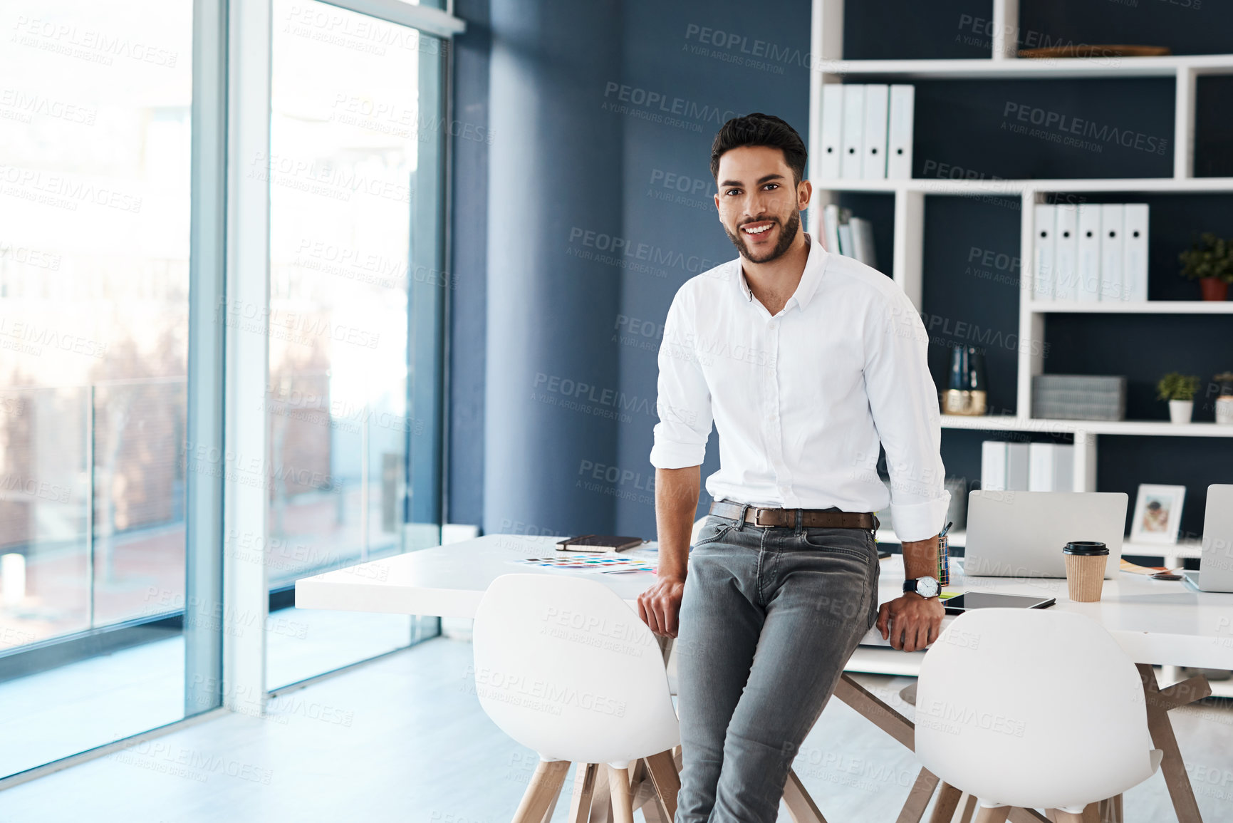 Buy stock photo Cropped portrait of a handsome young businessman sitting on his desk in his office alone