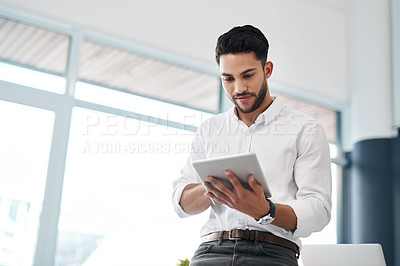 Buy stock photo Cropped shot of a handsome young businessman sitting alone in his office and using a tablet