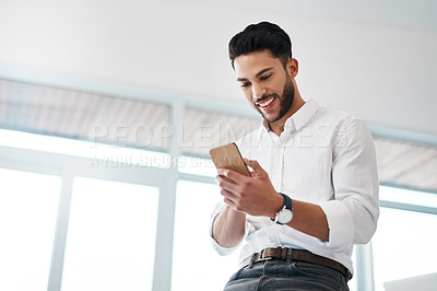 Buy stock photo Cropped shot of a handsome young businessman sitting alone in his office and texting on his cellphone