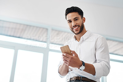Buy stock photo Cropped portrait of a handsome young businessman sitting alone in his office and texting on his cellphone