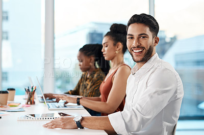 Buy stock photo Cropped portrait of a handsome young businessman sitting in the office while his colleagues work on laptops behind him