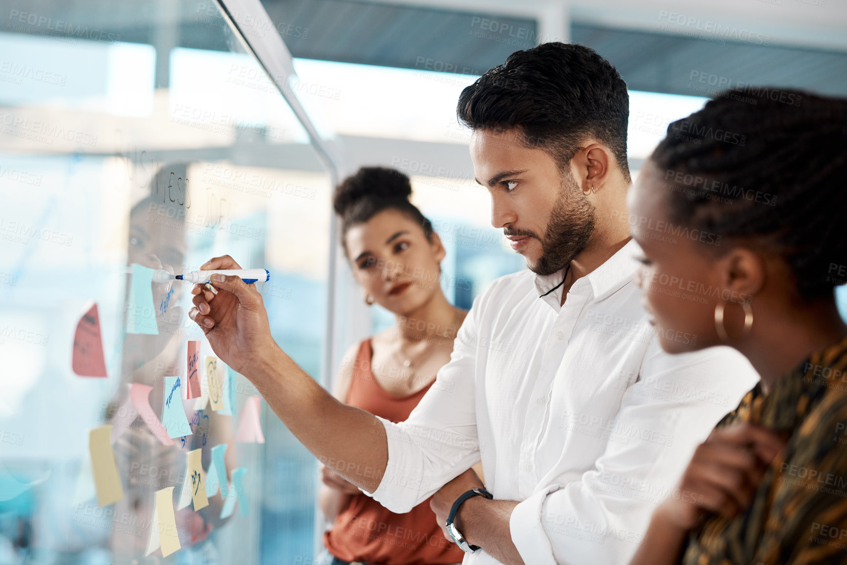 Buy stock photo Cropped shot of a diverse group of businesspeople standing and using a glass board with post-its in the office