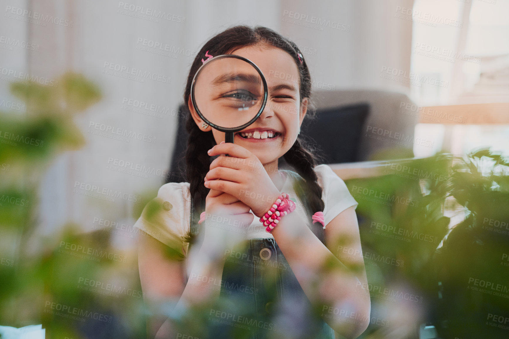 Buy stock photo Cropped portrait of an adorable little girl smiling while looking through a magnifying glass at home