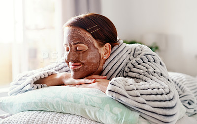 Buy stock photo Cropped shot of an attractive young woman lying on her bed with a mud mask on her face in the morning at home