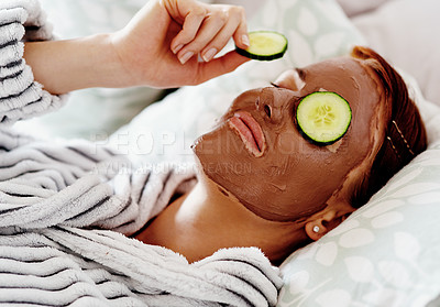 Buy stock photo Cropped shot of an attractive young woman placing a slice of cucumber on her face while pampering herself in her bedroom at home