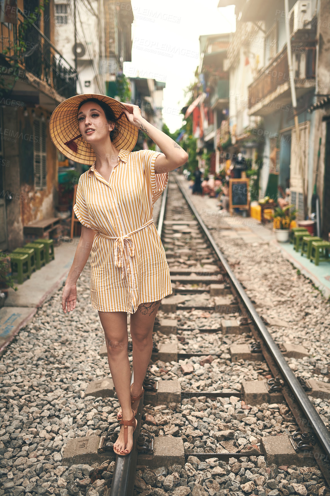 Buy stock photo Shot of a young woman walking on a train tracks through the streets of Vietnam