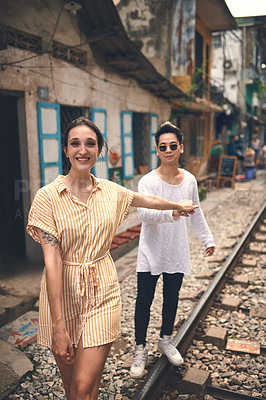 Buy stock photo Couple, portrait and smile with walking on train tracks in Vietnam for travel adventure, local experience or love. Tourist attraction, interracial people and holding hands on railroad for sightseeing